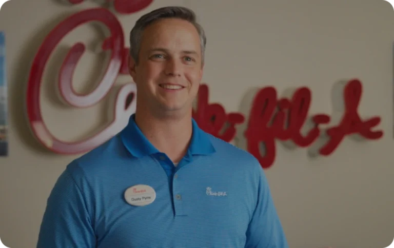 Dusty Pynes, a Chick-fil-A employee, smiling in front of the Chick-fil-A logo.
